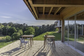 A wooden deck with two tables and chairs, overlooking a lush landscape.
