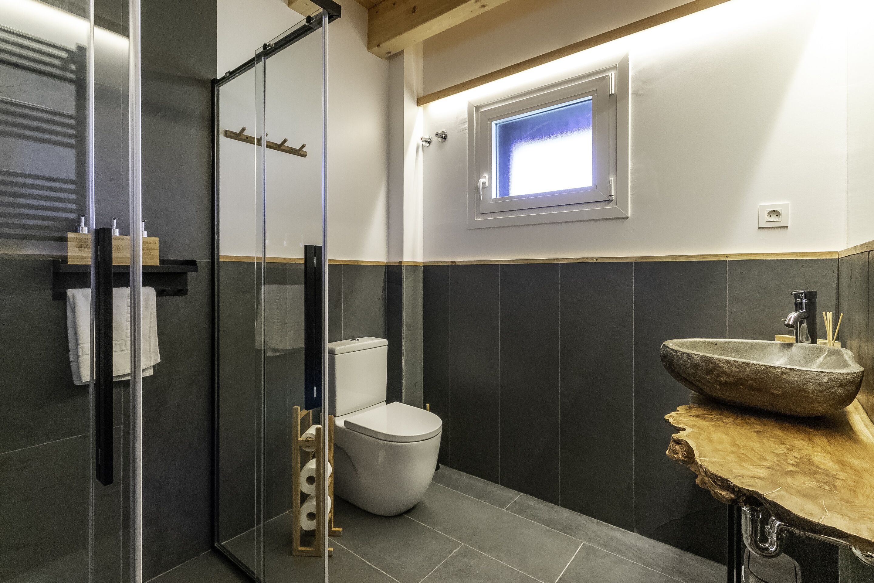 Un baño moderno con cabina de ducha de vidrio, inodoro y un lavamanos de piedra grande.