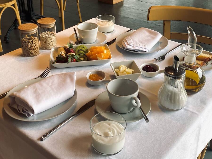 Una mesa de desayuno preparada con diversos alimentos, utensilios y una cafetera.