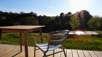 A wooden deck with a metal chair and a table, overlooking a swimming pool and trees.