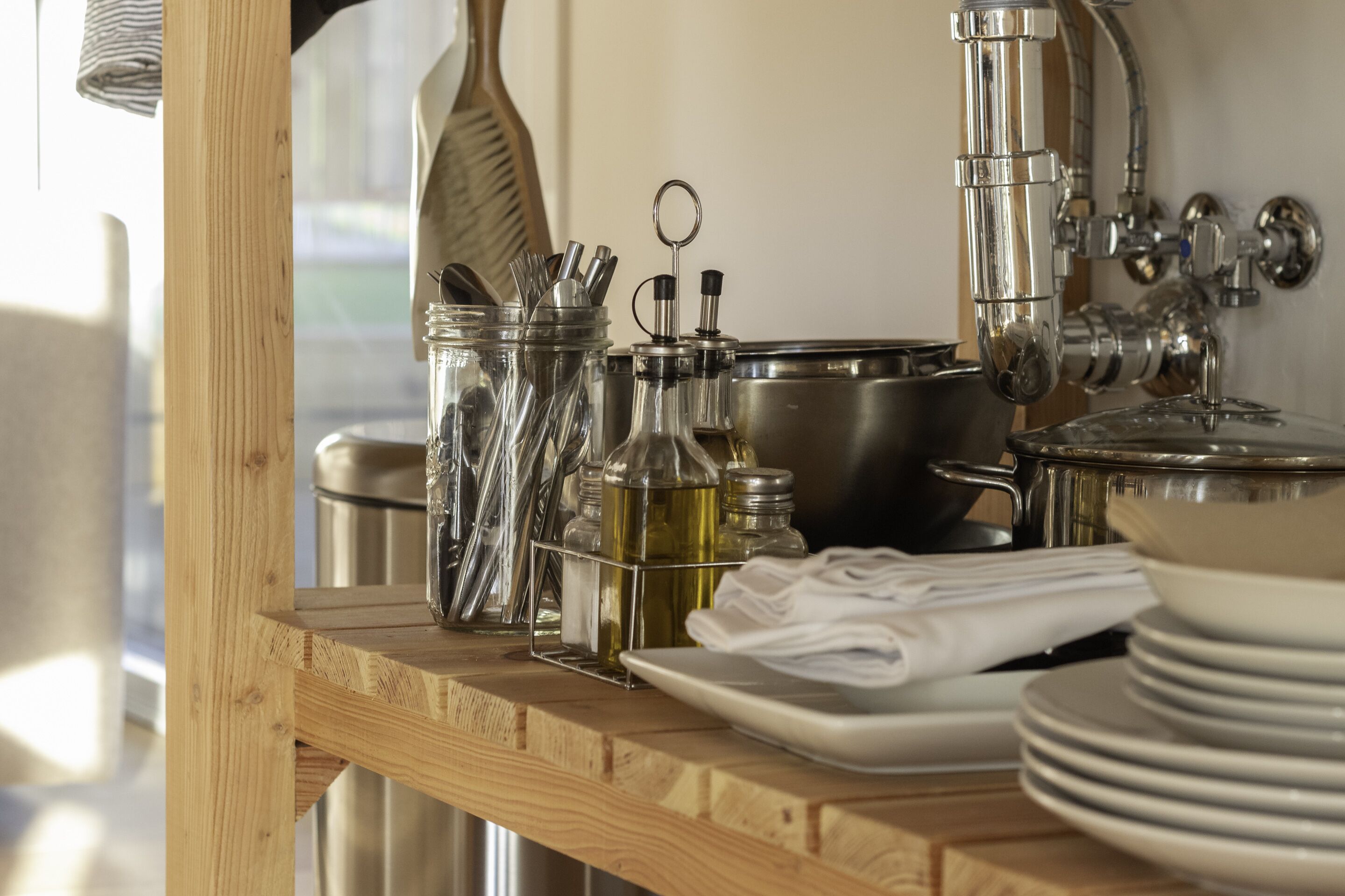A kitchen counter with stainless steel appliances, a wooden shelf, and stacked white plates.