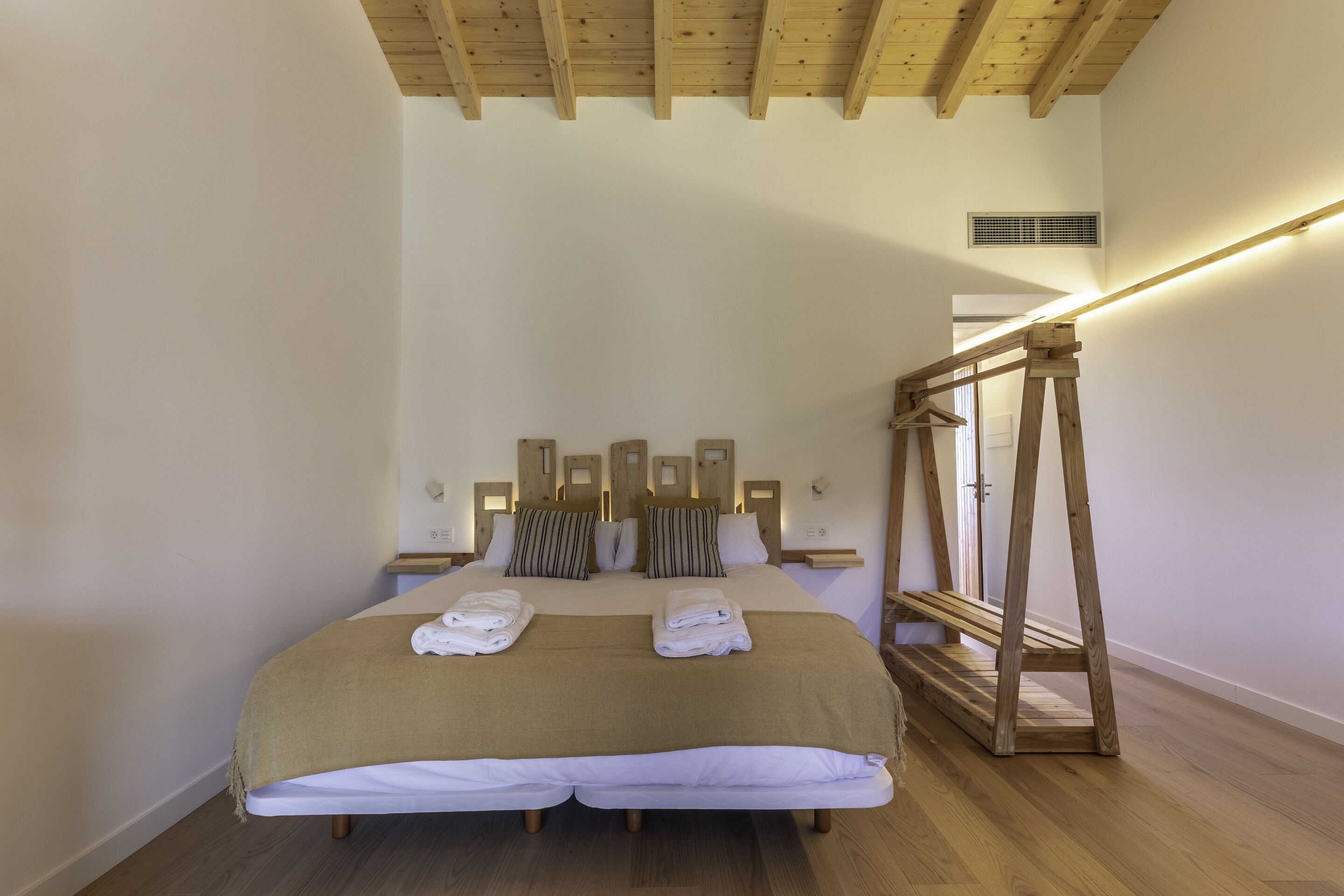 Un dormitorio con techo de madera, una cama con cabecera, mesitas de noche y una escalera de madera.