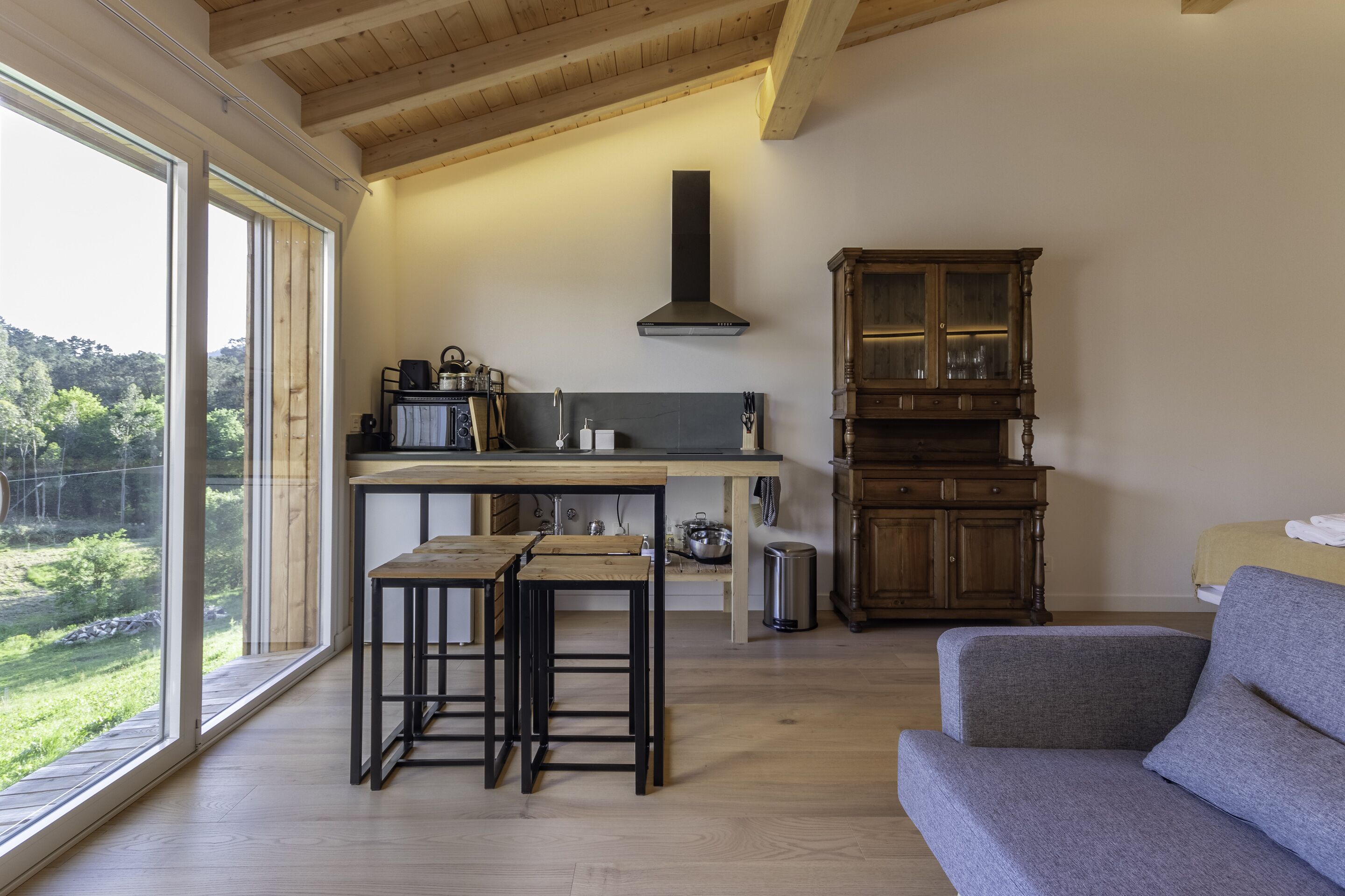 Une cuisine moderne avec des poutres en bois, une grande fenêtre et une vue sur la verdure.