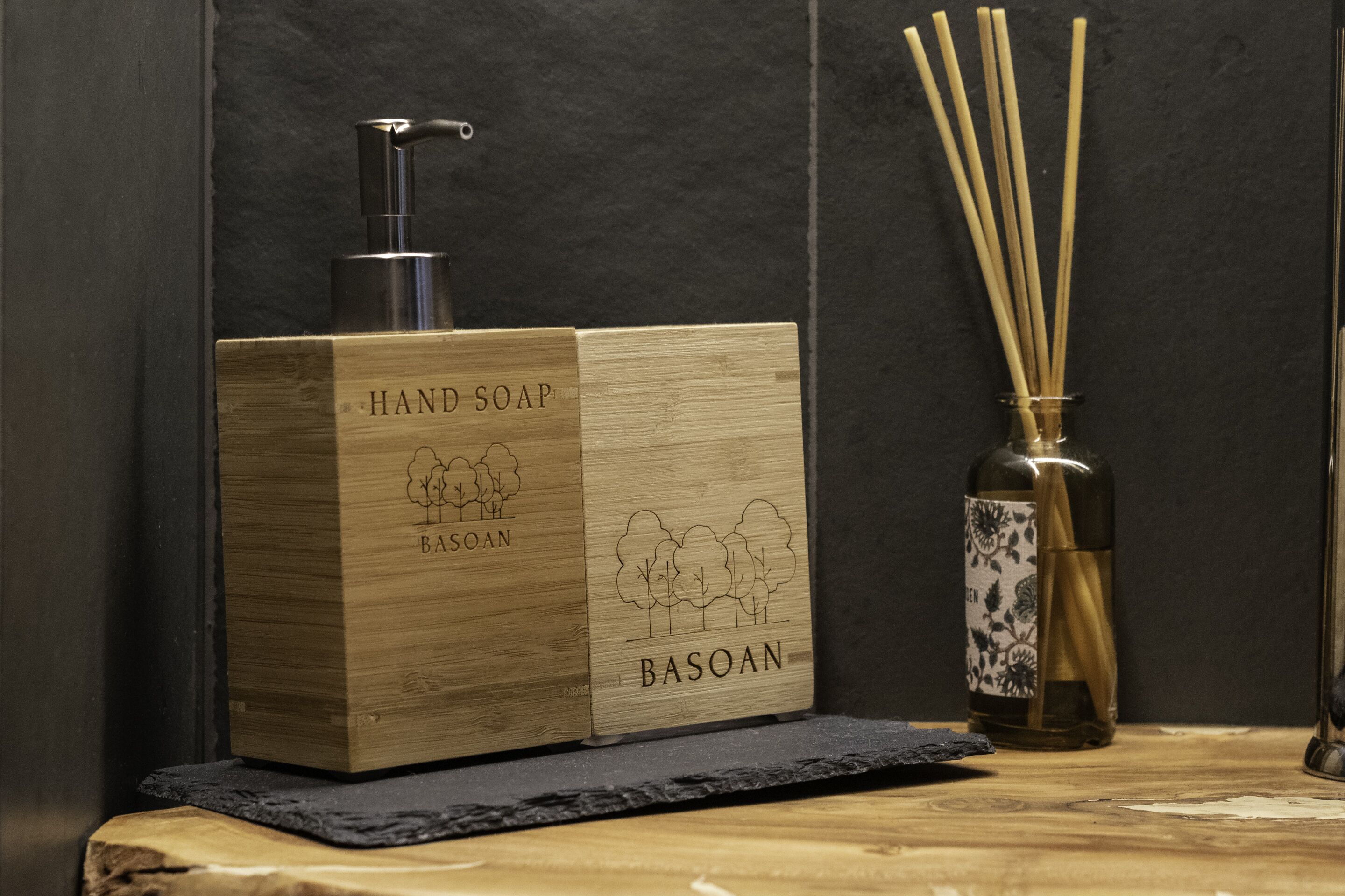 Een houten zeepdispenser met pomp, een bamboe re diffuser en een fles met een bloemmotief.