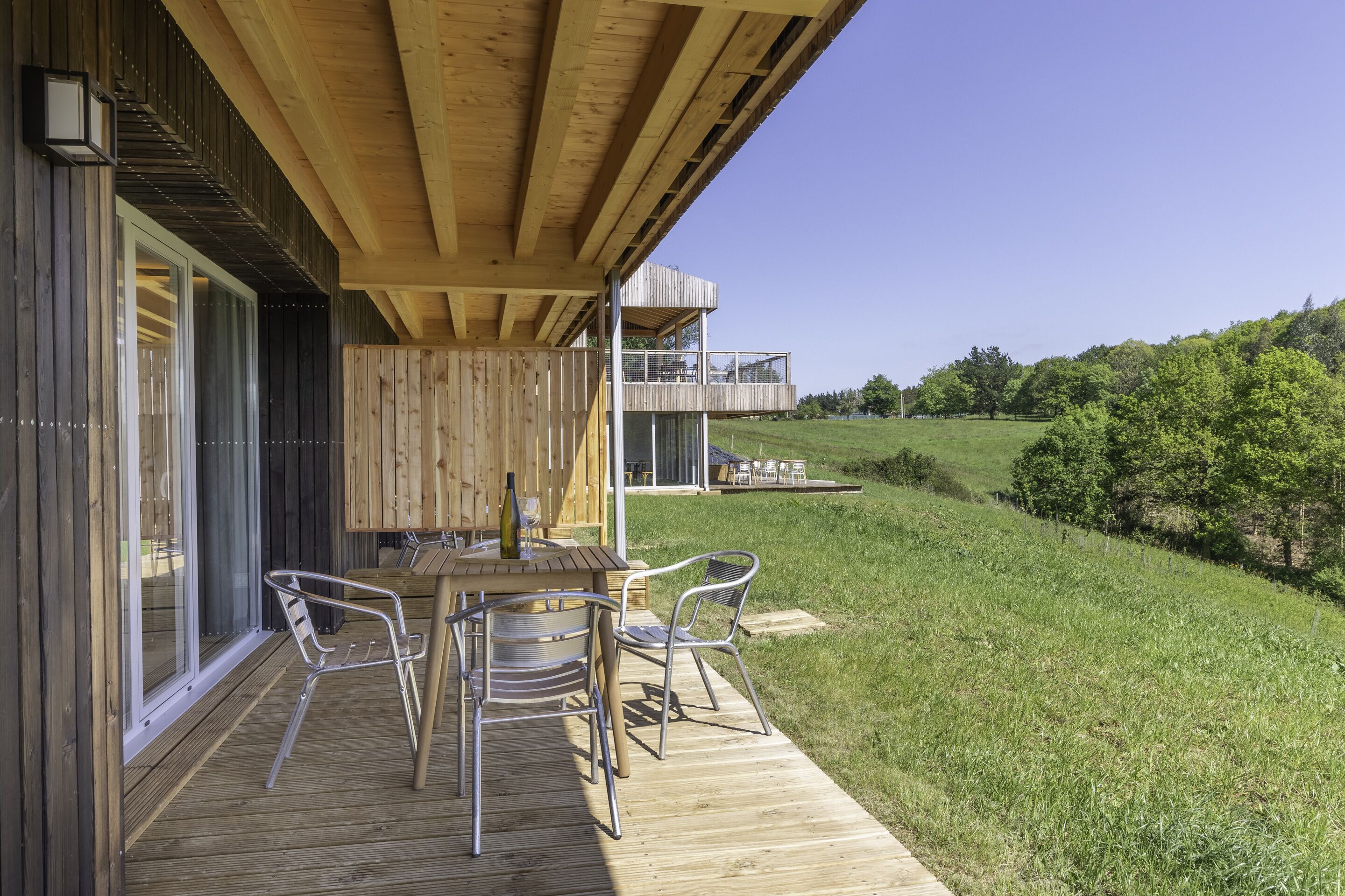 Un ponte in legno con tavolo e sedie, affacciato su una zona verde e un edificio con un balcone.