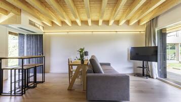 A modern living room with a wooden ceiling, a grey sofa, a wooden dining table with chairs, and a flat-screen TV.