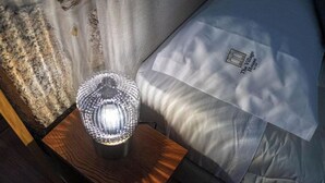 Eine Lampe auf einem Holztisch neben einem Bett mit einem Kissen, das ein Logo zeigt.