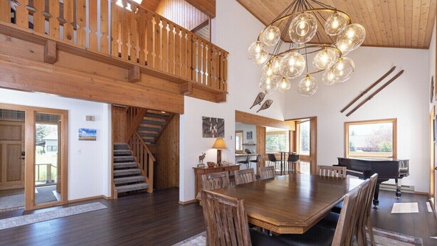 A spacious dining area with a large wooden table and chairs, a chandelier, and a piano. - Alpenglow Retreat | Big Sky Town | Sleeps 12! (Big Sky)