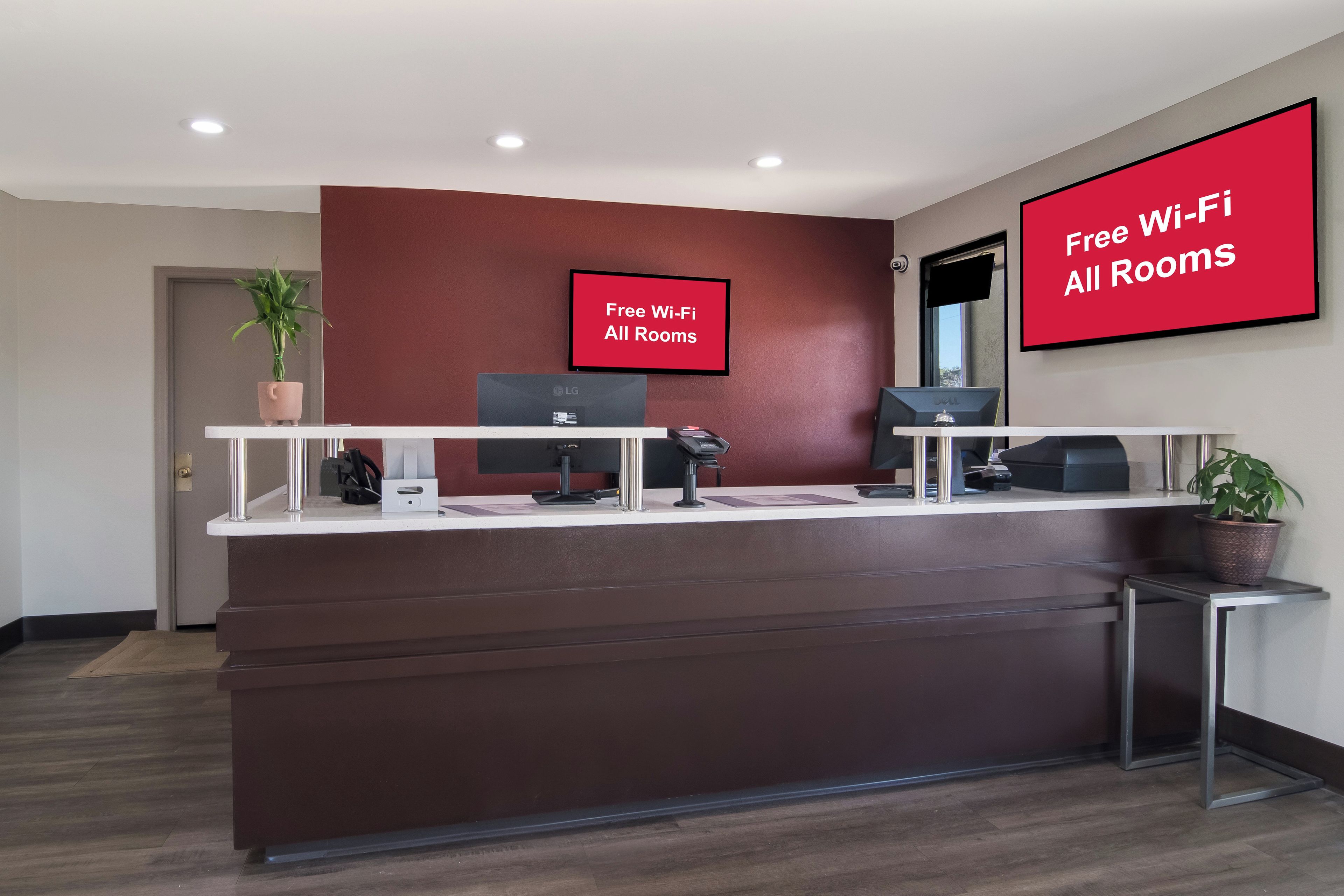 Un comptoir d’accueil avec un mur rouge, deux écrans d’ordinateur, un téléphone et un panneau indiquant : « Wi-Fi gratuit dans toutes les chambres ».