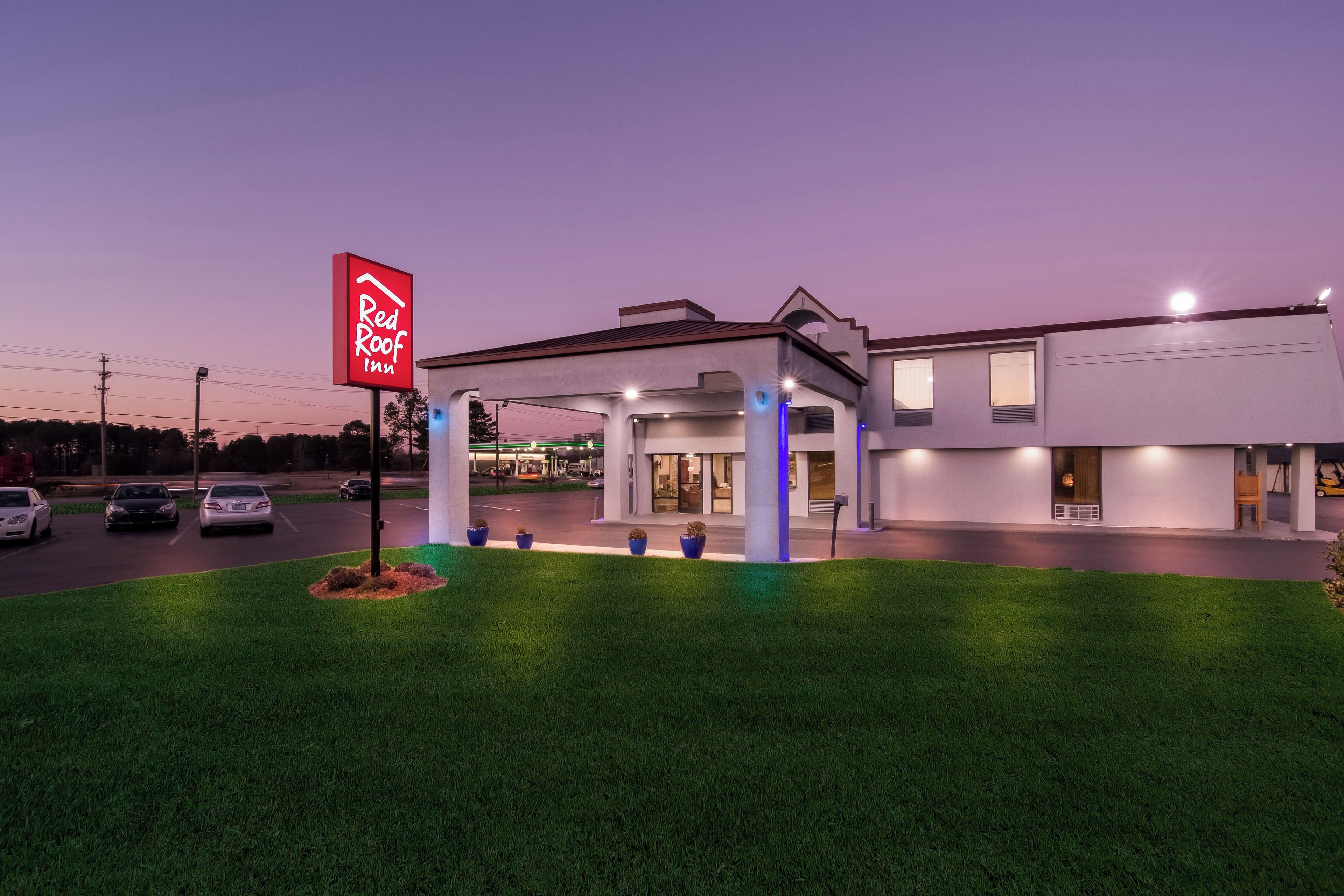 Un Red Roof Inn con diseño moderno, que cuenta con una zona de estacionamiento techada y un césped bien cuidado.