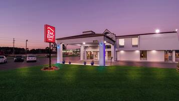 Un Red Roof Inn con diseño moderno, que cuenta con una zona de estacionamiento techada y un césped bien cuidado.