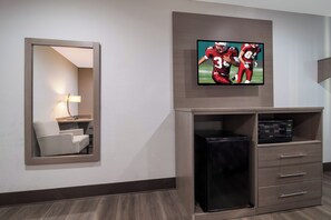 Habitación de hotel con una televisión de pantalla plana sobre una minibar, un espejo y una zona de estar con una lámpara.