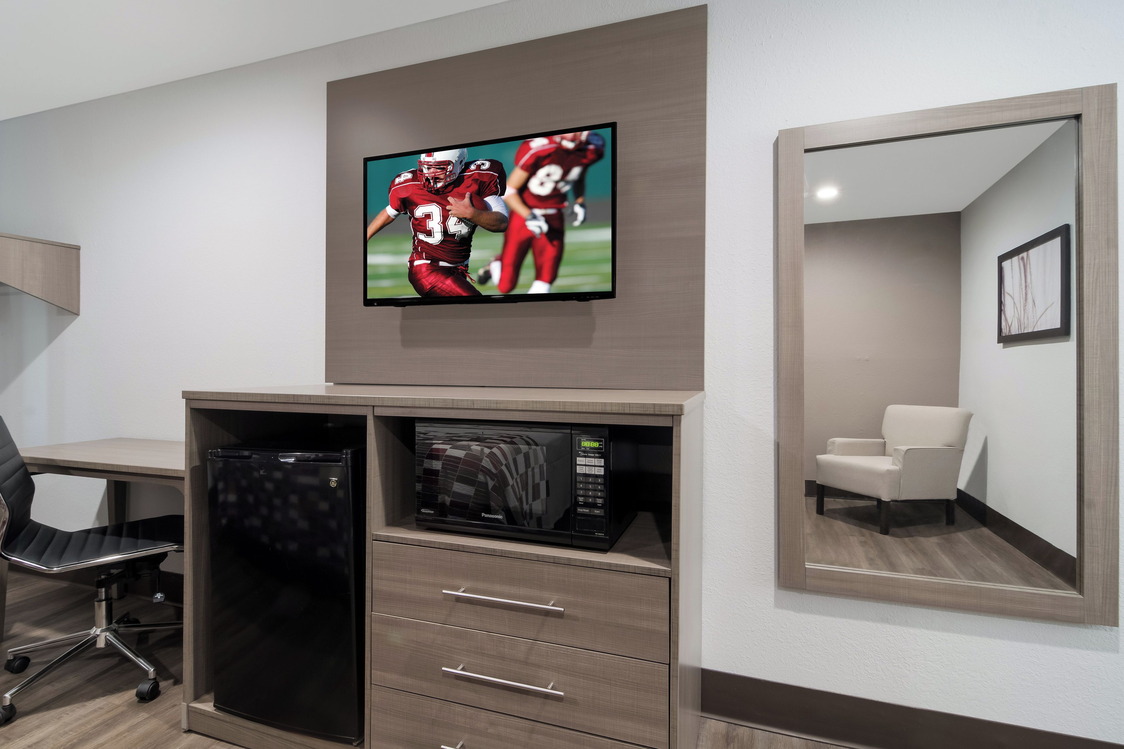 Habitación de hotel con televisor de pantalla plana sobre un mueble de madera, un microondas y un refrigerador pequeño.