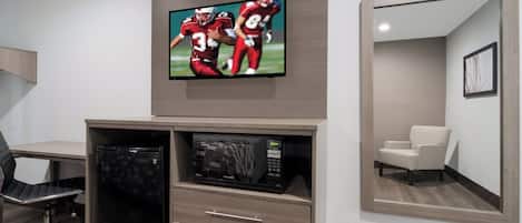 Habitación de hotel con televisor de pantalla plana sobre un mueble de madera, un microondas y un refrigerador pequeño.