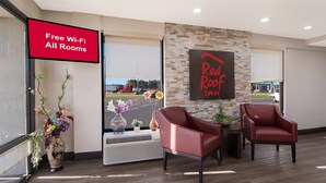 A hotel lobby with a 'Free Wi-Fi All Rooms' sign, a 'Red Roof Inn' sign, and two red armchairs. - Red Roof Inn Rocky Mount - Battleboro (Battleboro)