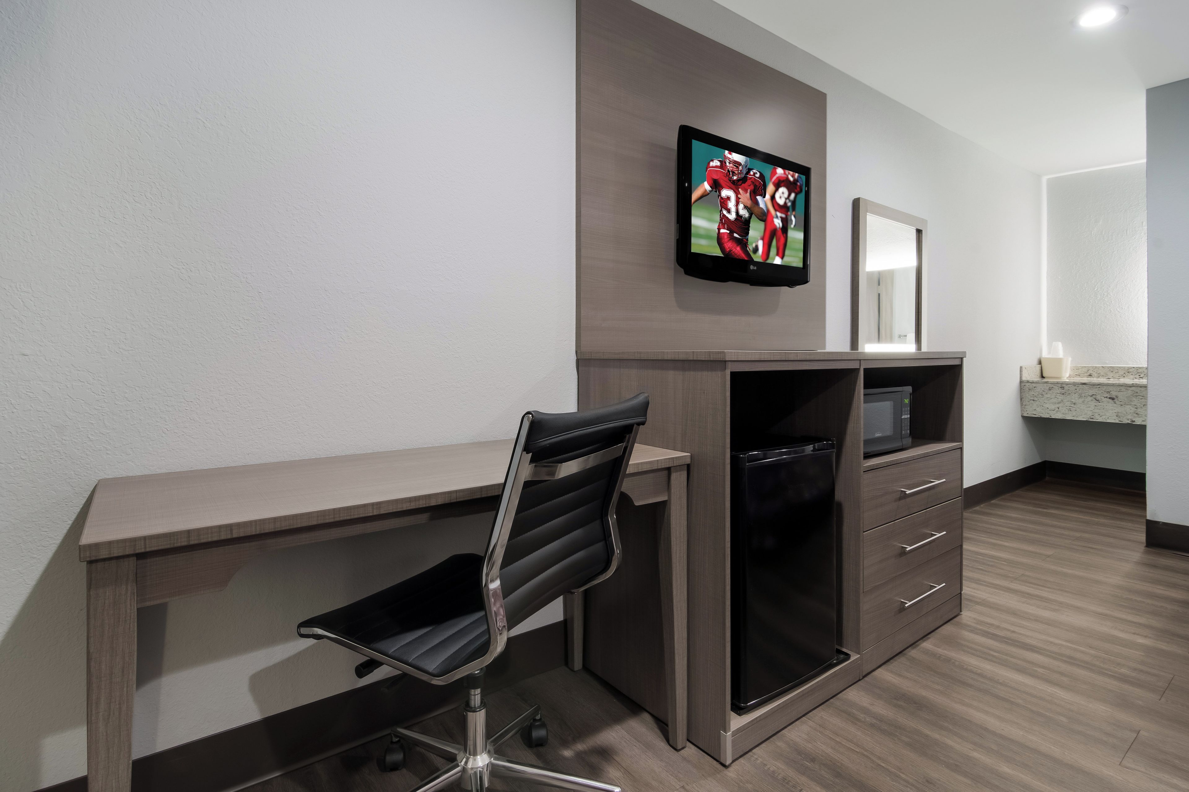 Un espace de bureau moderne comprenant un bureau, une chaise, un téléviseur et un four à micro-ondes.