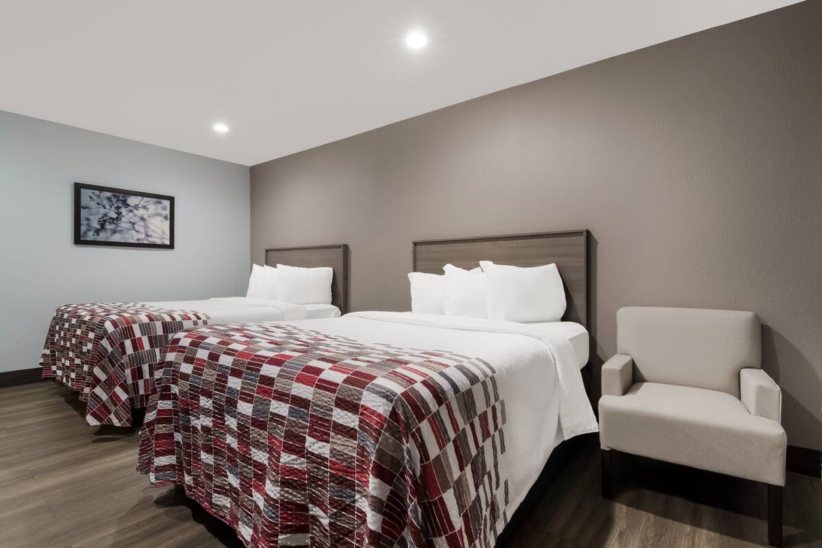 A hotel room with two beds, a chair, and a framed picture on the wall.