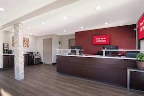 A hotel reception area with a modern design, including a reception desk, a coffee machine, and a digital screen displaying 'Free Wi-Fi All Rooms'. - Red Roof Inn Rocky Mount - Battleboro (Battleboro)