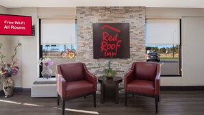 A Red Roof Inn reception area with two red leather chairs, a stone wall, and a large window. - Red Roof Inn Rocky Mount - Battleboro (Battleboro)