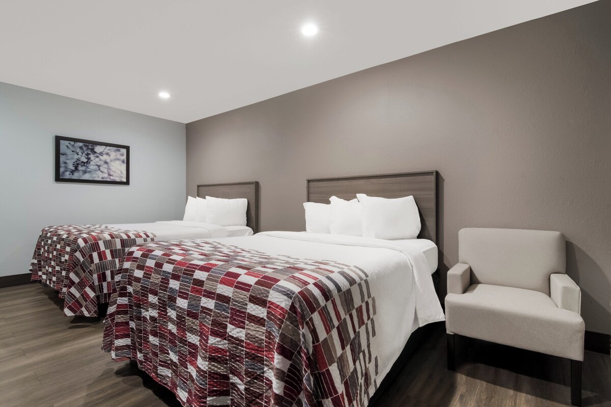 Een hotelkamer met twee bedden, een stoel en een ingelijst foto aan de muur.