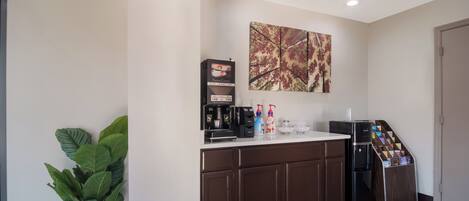 A kitchenette with a coffee machine, a plant, and a coffee dispenser.