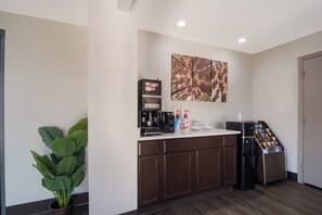 Una kitchenette con cafetera, una planta y dispensador de café.
