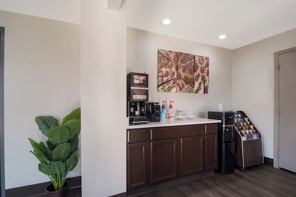A kitchenette with a coffee machine, a plant, and a coffee dispenser.
