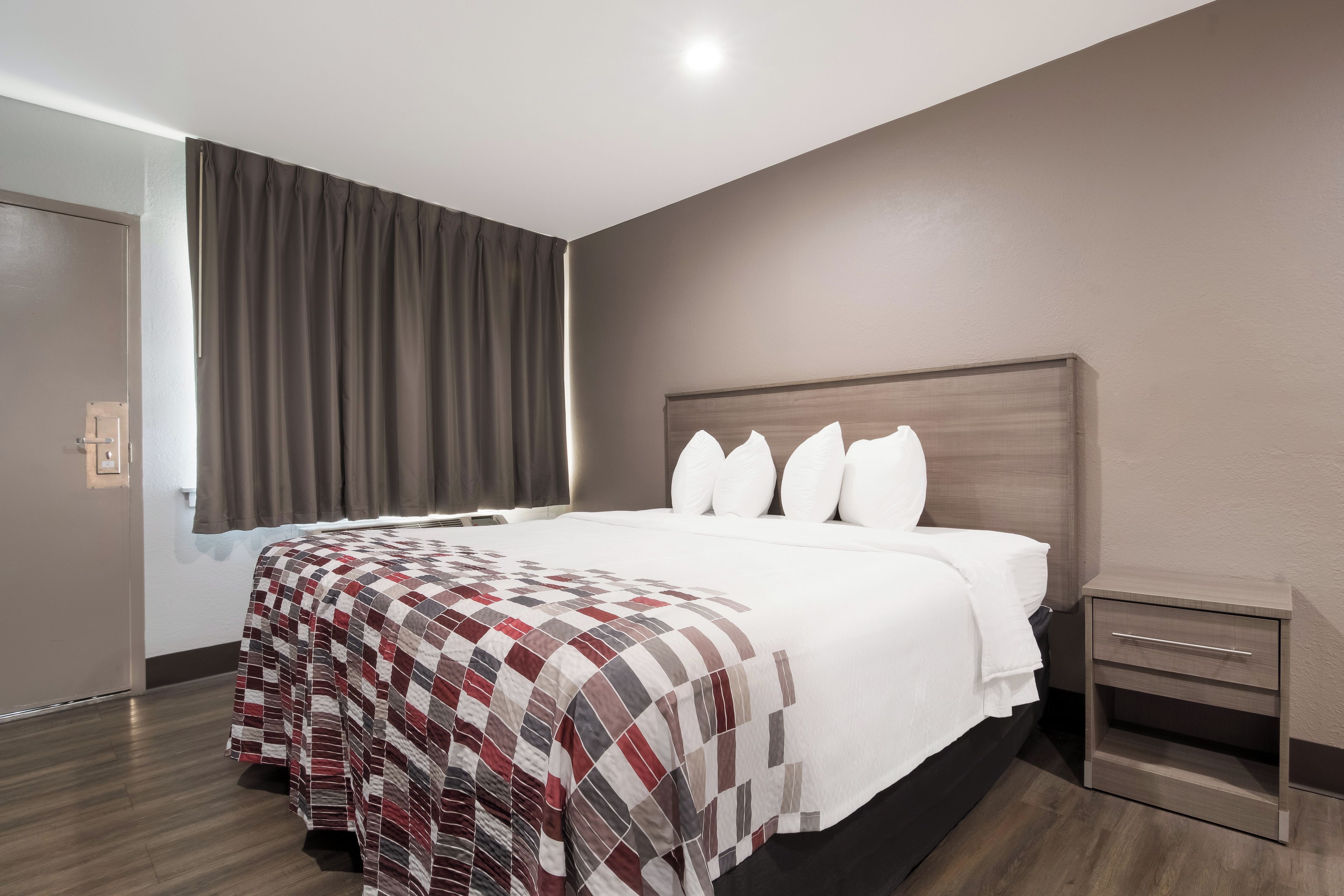 Una habitación de hotel con una cama grande, una mesita de noche y un ventanal con cortinas.