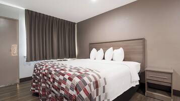 Una habitación de hotel con una cama grande, una mesita de noche y un ventanal con cortinas.