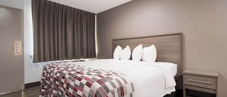 A hotel room with a large bed, a bedside table, and a window with curtains.