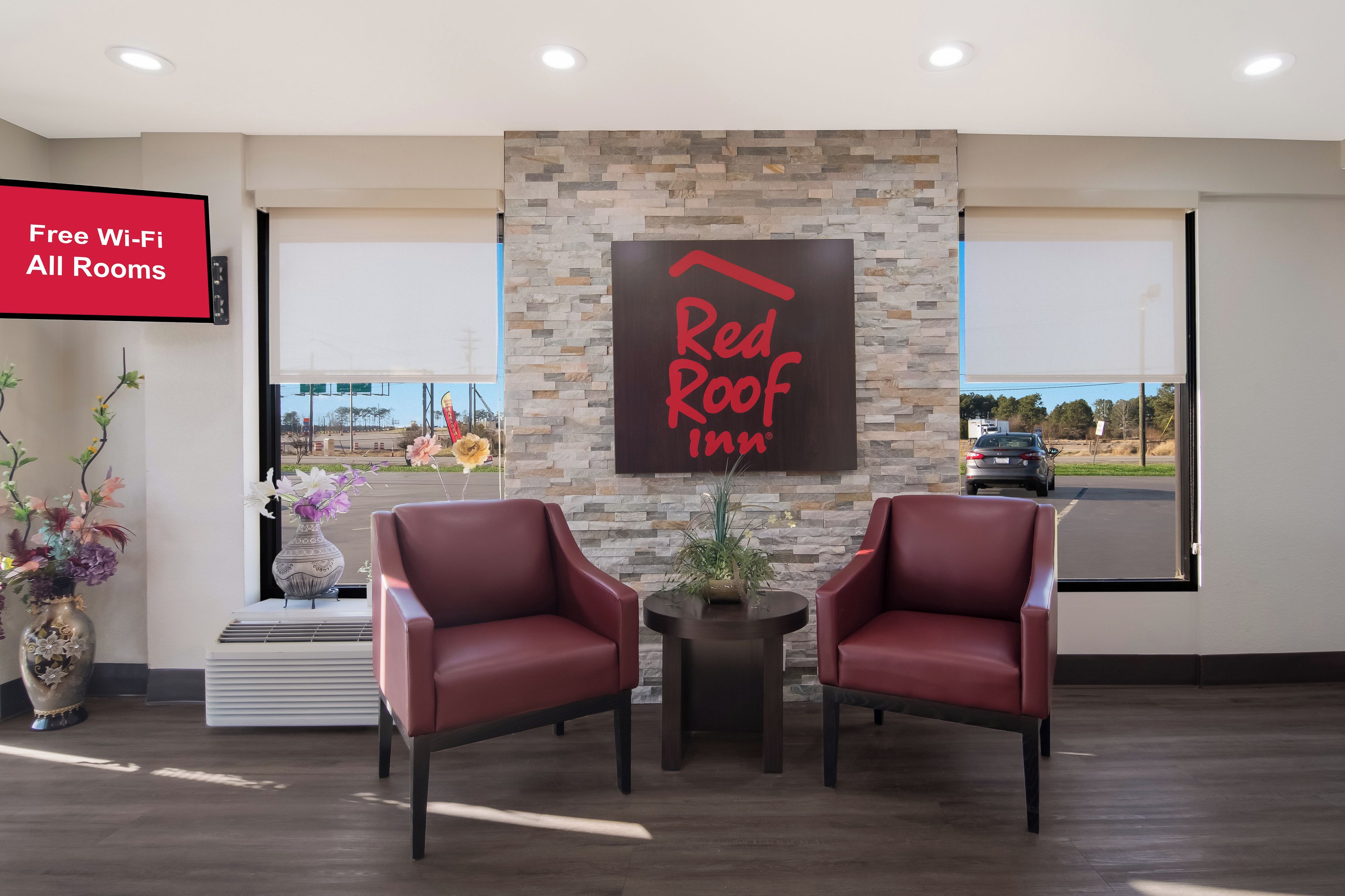 L’espace d’accueil d’un hôtel Red Roof Inn, avec deux fauteuils en cuir, un mur en pierre et un panneau indiquant que le Wi-Fi est gratuit dans toutes les chambres.