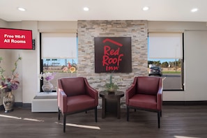 Zona de recepción de Red Roof Inn con dos sillones de cuero, una pared de piedra y un letrero que indica Wi-Fi gratuito en todas las habitaciones.