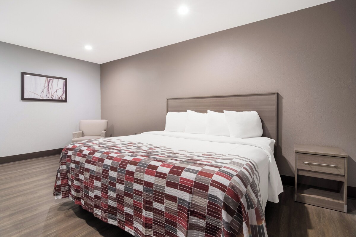 Een hotelkamer met een groot bed, een nachtkastje, een wandlamp en een ingelijst kunstwerk aan de muur.