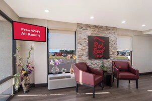 Un vestíbulo de hotel con un cartel que dice 'Wi-Fi gratuito en todas las habitaciones', un cartel de 'Red Roof Inn' y dos sillones rojos.