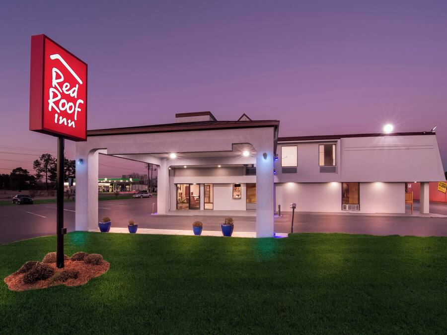 Un Red Roof Inn con un diseño moderno, que cuenta con estacionamiento techado y una entrada bien iluminada.
