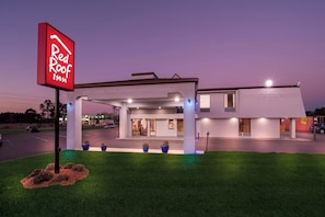 Un Red Roof Inn con un diseño moderno, que cuenta con estacionamiento techado y una entrada bien iluminada.