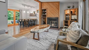 Un salon moderne avec une cheminée, des éléments décoratifs en bois et un coin repas agrémenté de tabourets de bar.