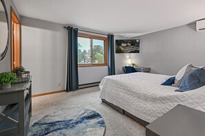 Ett sovrum med en säng, ett skrivbord, en stol, ett fönster med gardiner och en väggmonterad luftkonditioneringsanläggning.