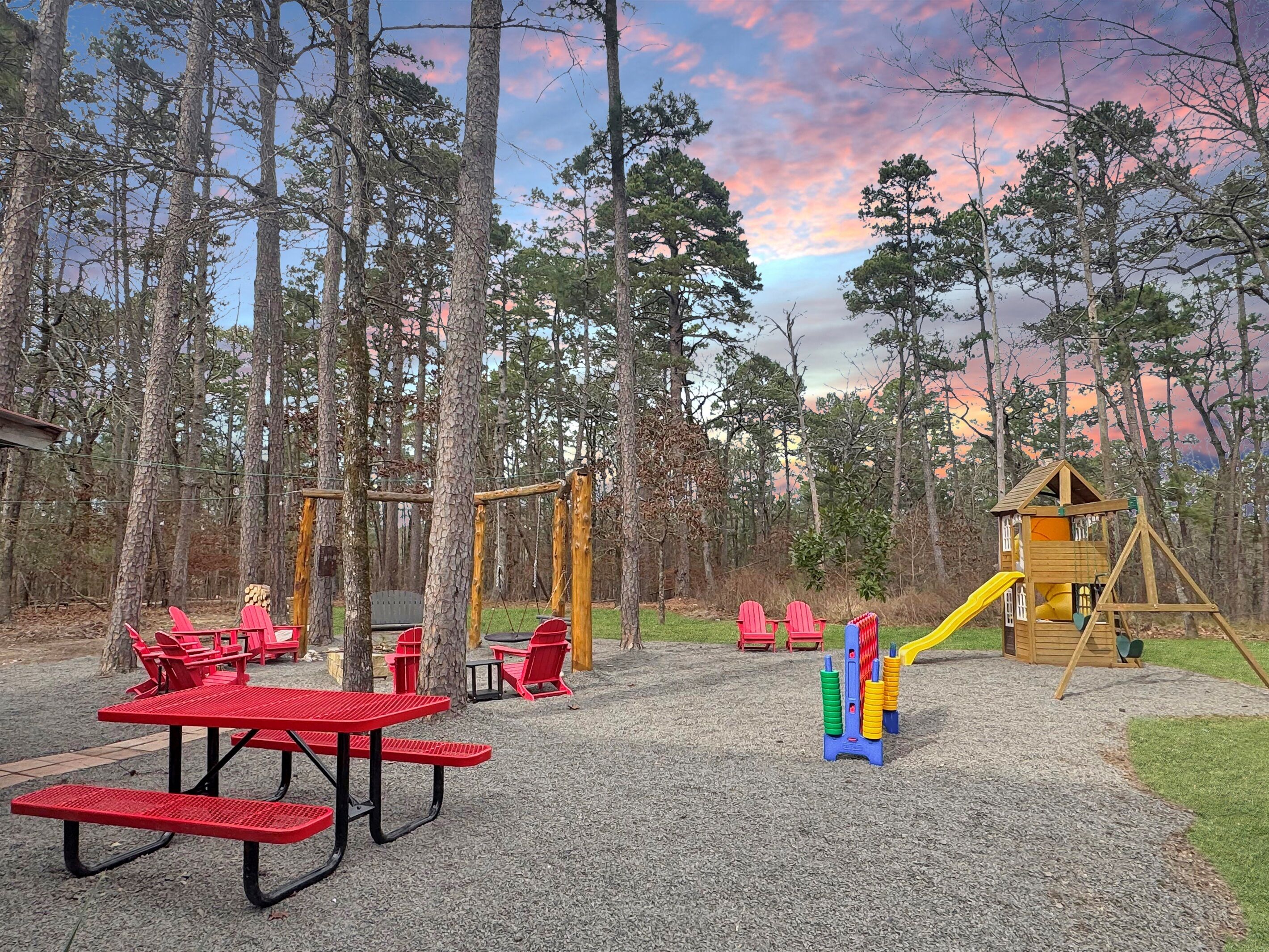 A playground with red picnic tables, a wooden swing set, and a playhouse with a slide.
