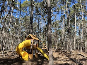 Explore a charming playhouse nestled among tall pine trees in a forest setting.