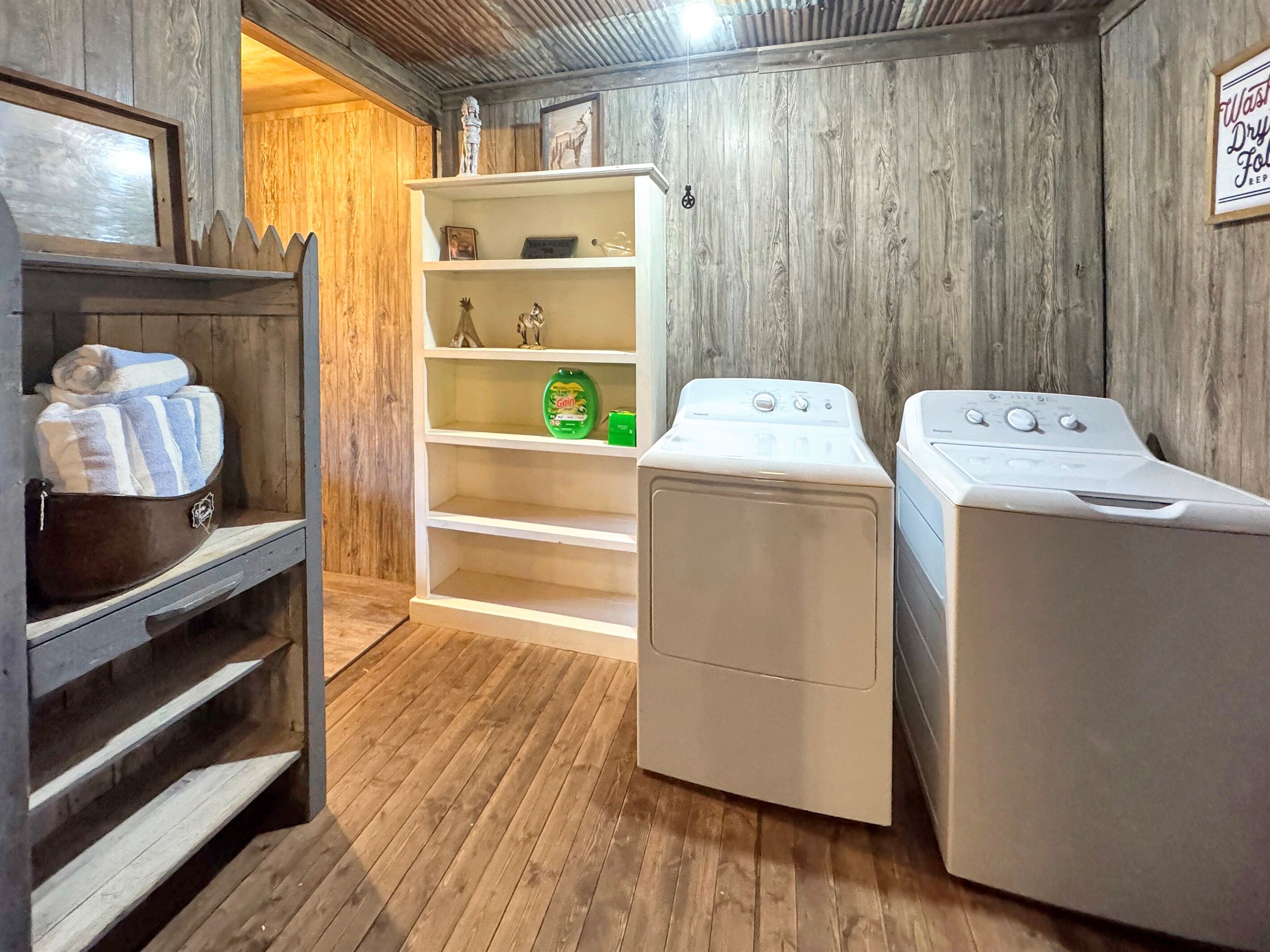 A laundry room with two washing machines, a shelf with towels, and a shelf with a detergent bottle.