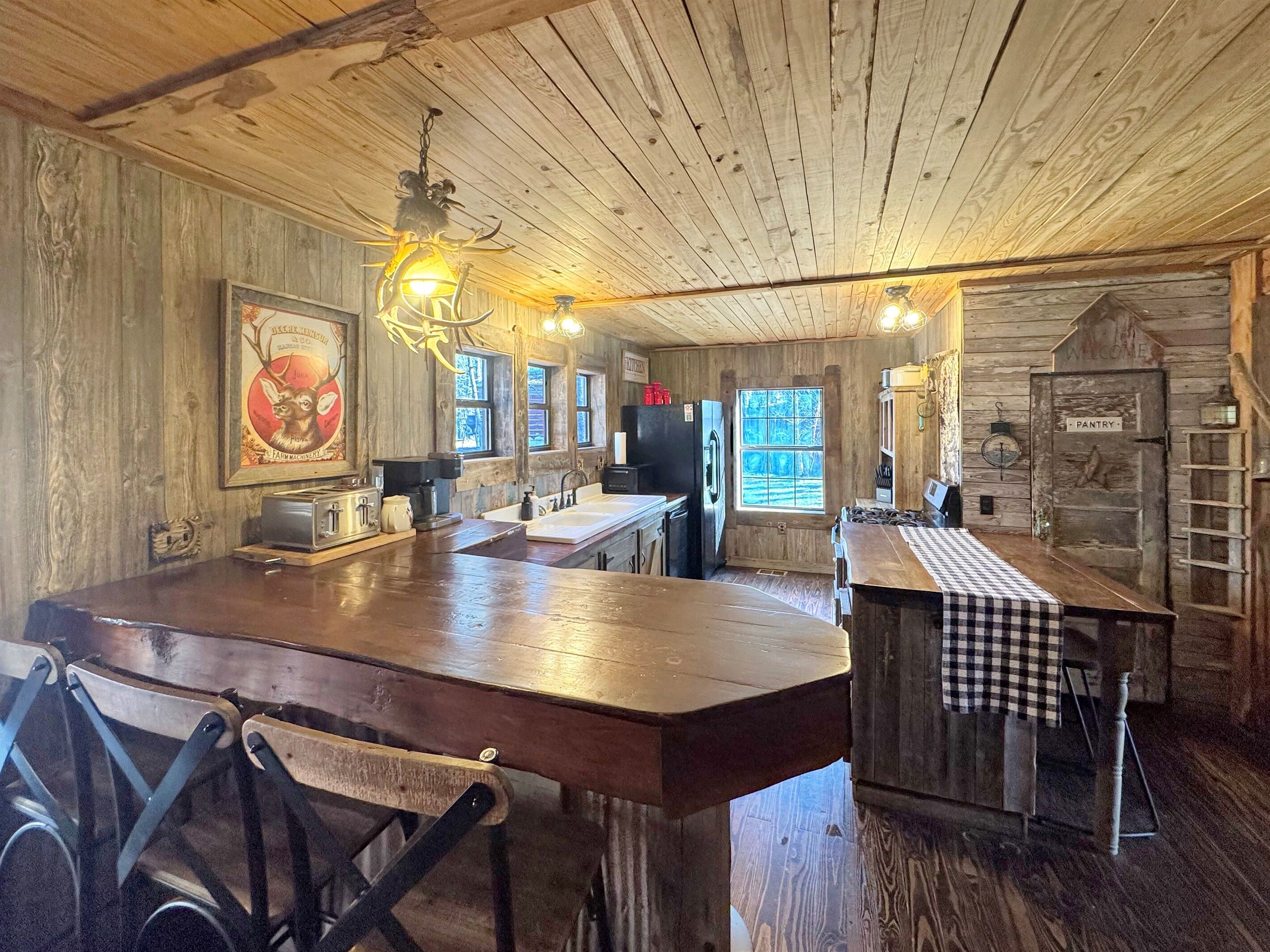 A rustic kitchen with wooden walls, a large island with a checkered tablecloth, and a vintage refrigerator.