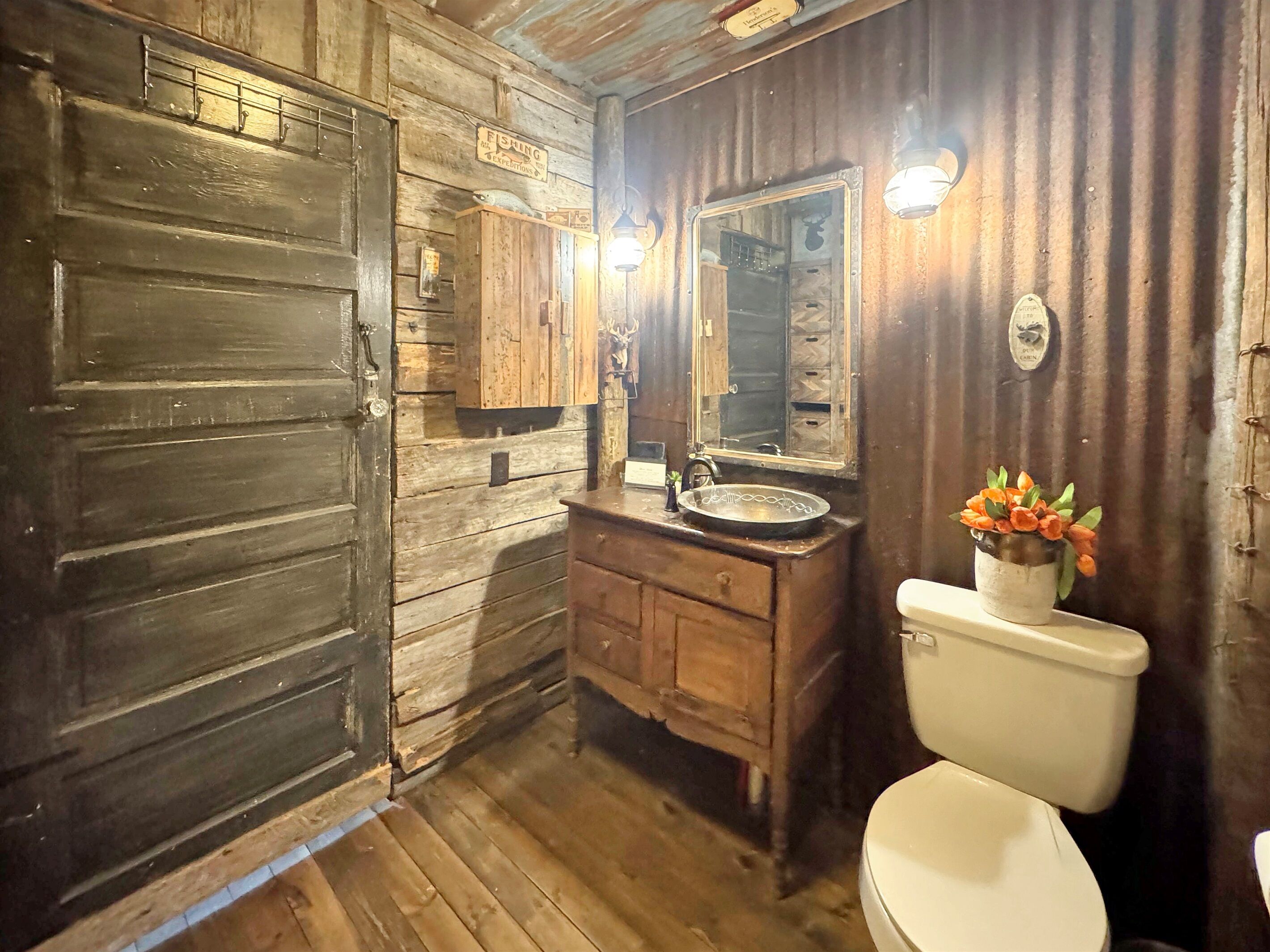 Une salle de bain rustique avec des murs en bois, un lavabo, des toilettes et un miroir.