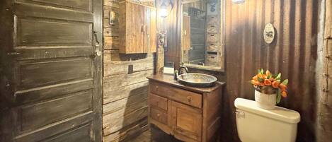 Une salle de bain rustique avec des murs en bois, un lavabo, des toilettes et un miroir.