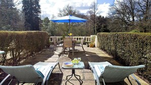 An outdoor patio with two lounge chairs, a table, and a blue umbrella.