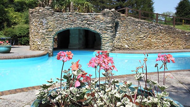 A stone archway leading to a pool area with a stone wall and greenery in the background.