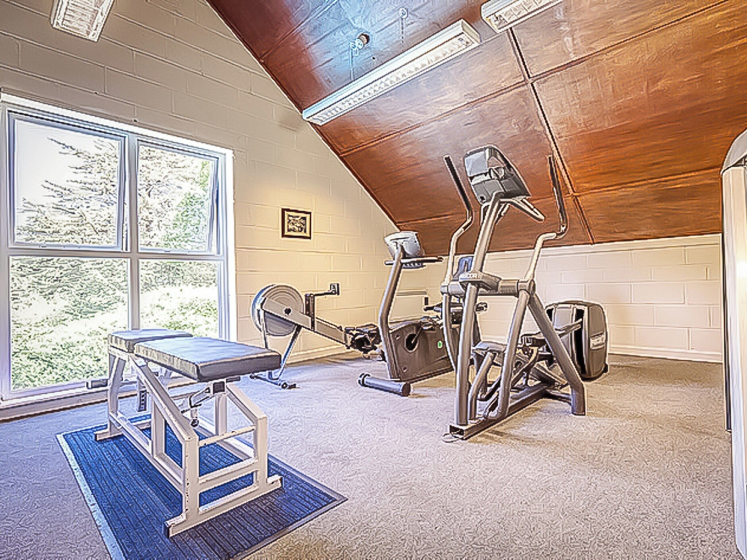 A gym with exercise equipment, a bench, and a large window providing natural light.