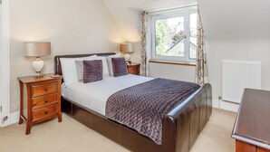 A bedroom with a bed, two bedside tables, a window with curtains, a radiator, and a chandelier. - Willow Cottage - Uk39244 (Inverness)