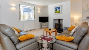 A modern living room with a fireplace, leather sofas, a glass coffee table, and a television. - Willow Cottage - Uk39244 (Inverness)
