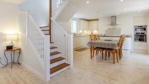 A modern kitchen with wooden flooring, a dining area with a table and chairs, and a staircase with white railings. - Willow Cottage - Uk39244 (Inverness)